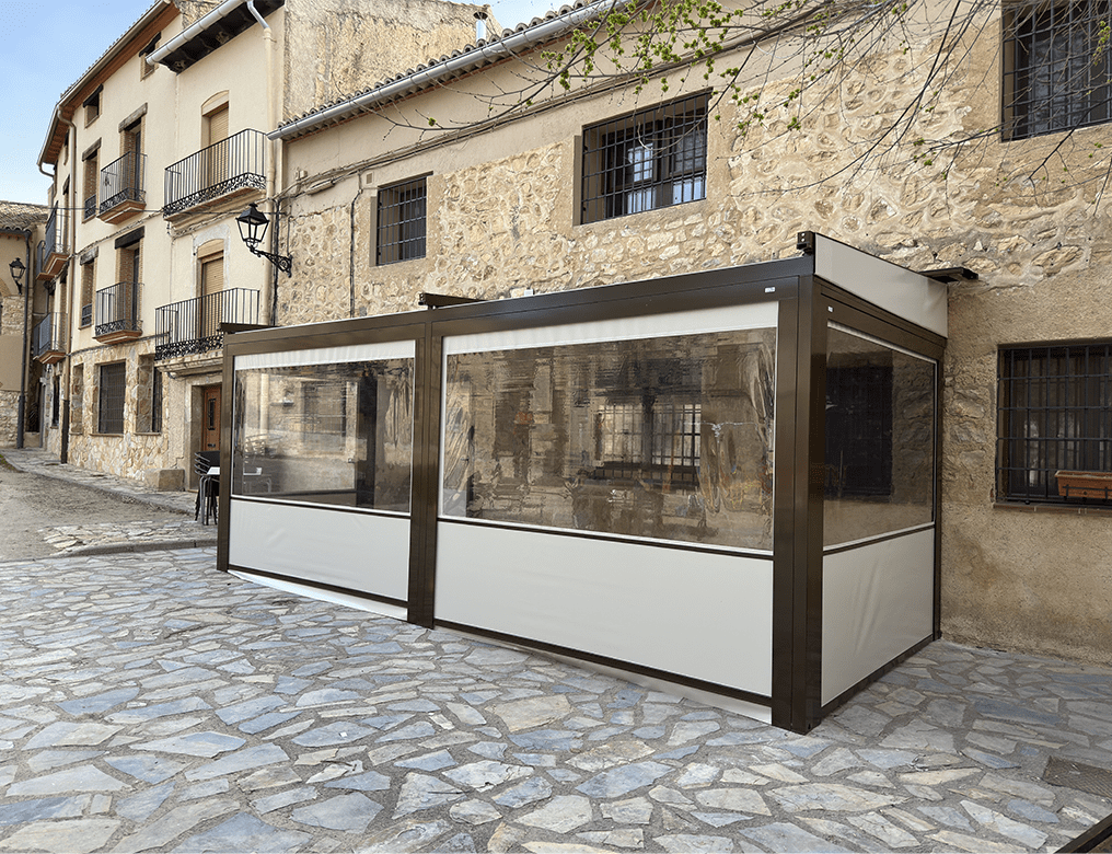 Cerramiento de terraza con estructura metálica y paneles transparentes en fachada rústica – instalación de Toldos Ángel